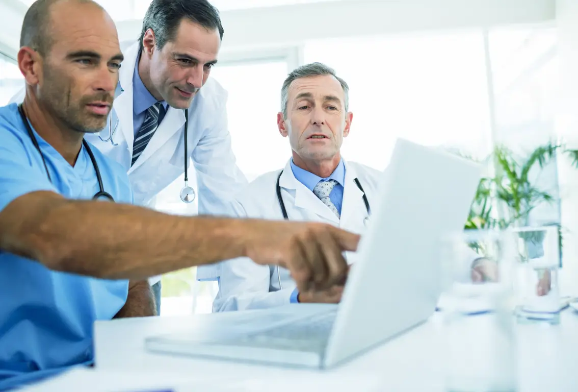 Profesionales de la salud colaborando y revisando información en un portátil.