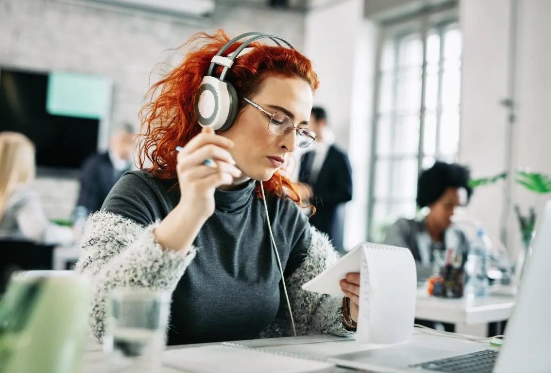 Una mujer con auriculares trabajando en un portátil en un entorno de oficina, concentrada y absorta en una sesión remota.