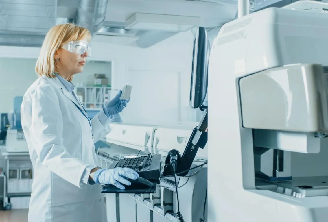 Científica con bata de laboratorio y gafas de seguridad operando un equipo de laboratorio avanzado, lo que sugiere precisión y análisis de alta tecnología.