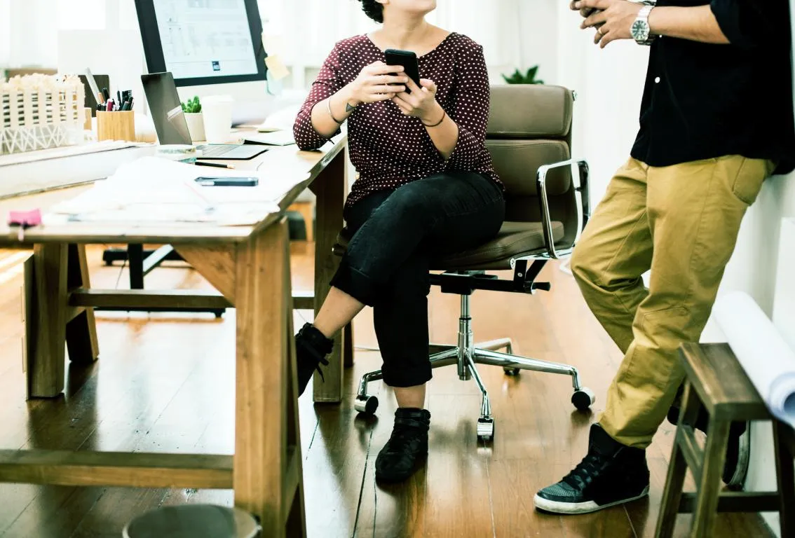 Dos personas en un entorno de oficina, una mirando la pantalla de un ordenador, sugiriendo colaboración o trabajo concentrado en un espacio de trabajo moderno.