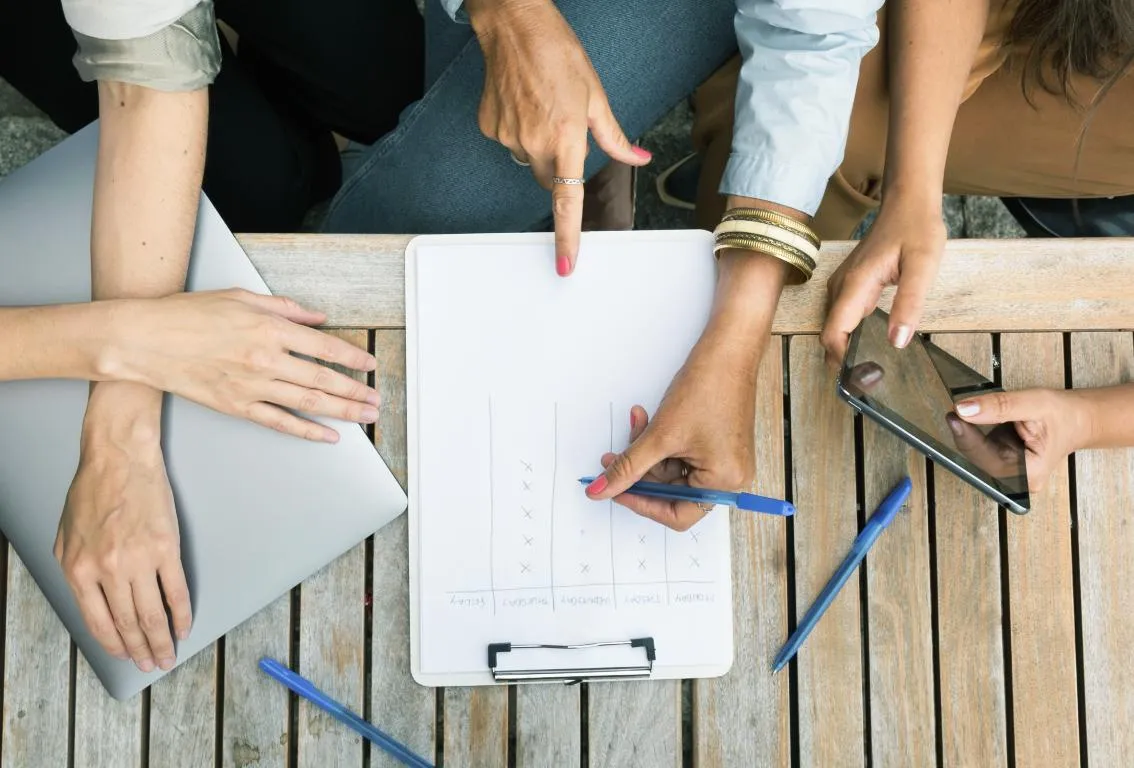 Varias manos, probablemente de un equipo, colaborando alrededor de una tableta y documentos, simbolizando trabajo en equipo y tecnología.