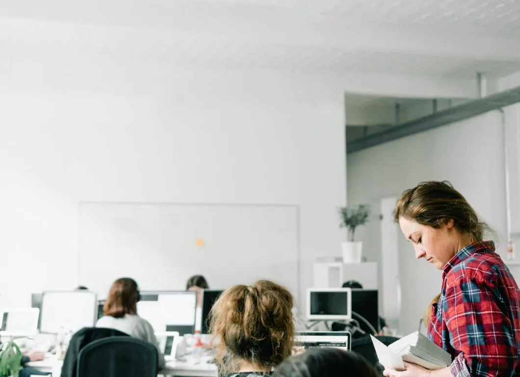 Un espacio de oficina moderno y de planta abierta con varias personas trabajando en escritorios con ordenadores, sugiriendo un ambiente de trabajo colaborativo y productivo.